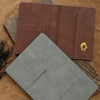 A brown leather passport holder and a gray leather cardholder are displayed on a textured brown surface.