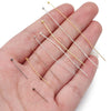 A hand holds several gold-plated brass ball head pins for jewelry making, showing various lengths and finishes.