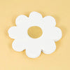 A white, flower-shaped disposable party item with a cutout center is shown on a light beige surface.
