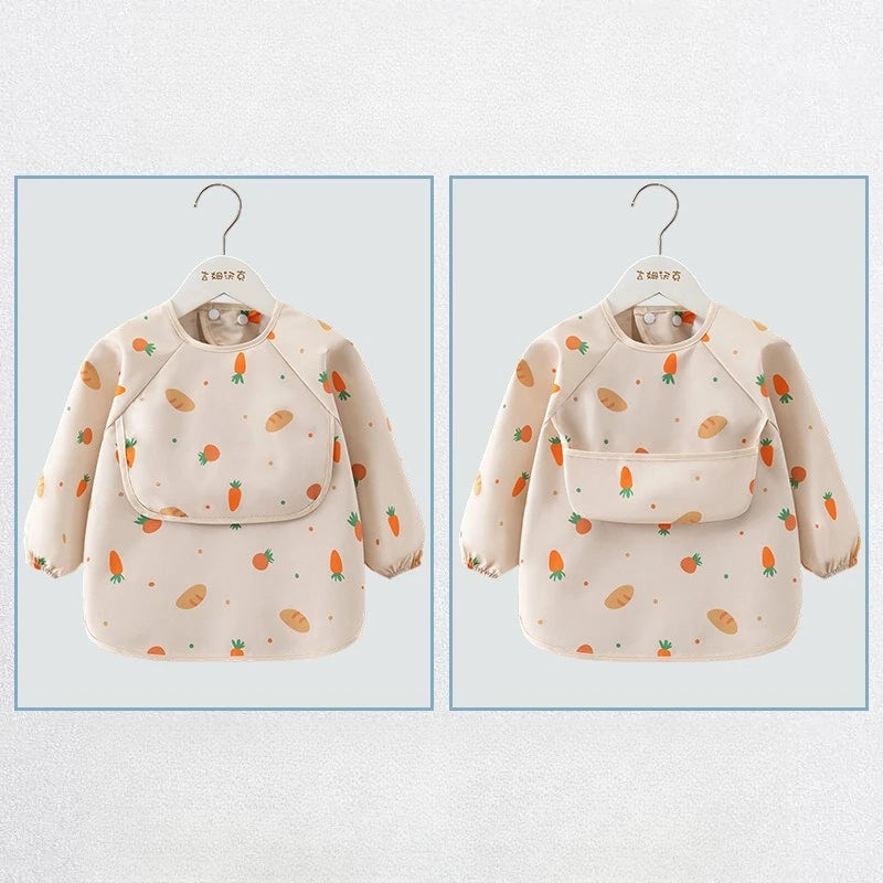 A beige long sleeve feeding bib for a child with a catch pocket, featuring an all-over pattern of carrots and fruit.