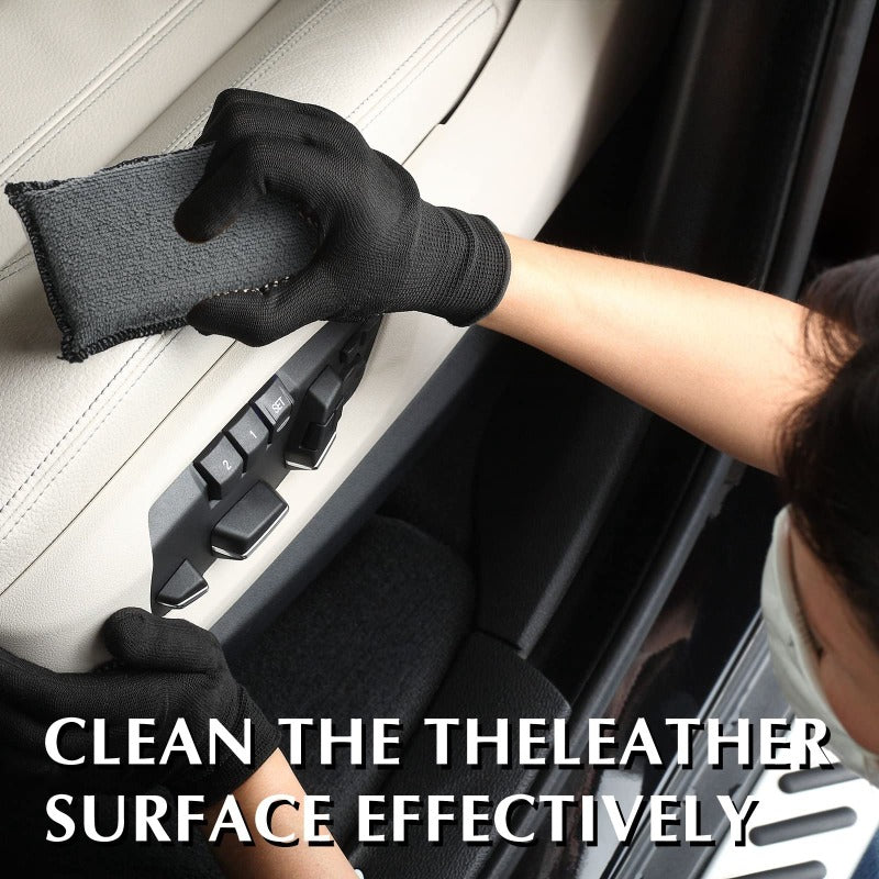 A hand wearing a black glove cleans the leather surface of a car interior with a microfiber sponge.