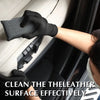 A hand wearing a black glove cleans the leather surface of a car interior with a scrubbing sponge.