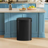 A sleek black automatic touchless trash can sitting on a light-colored kitchen countertop.