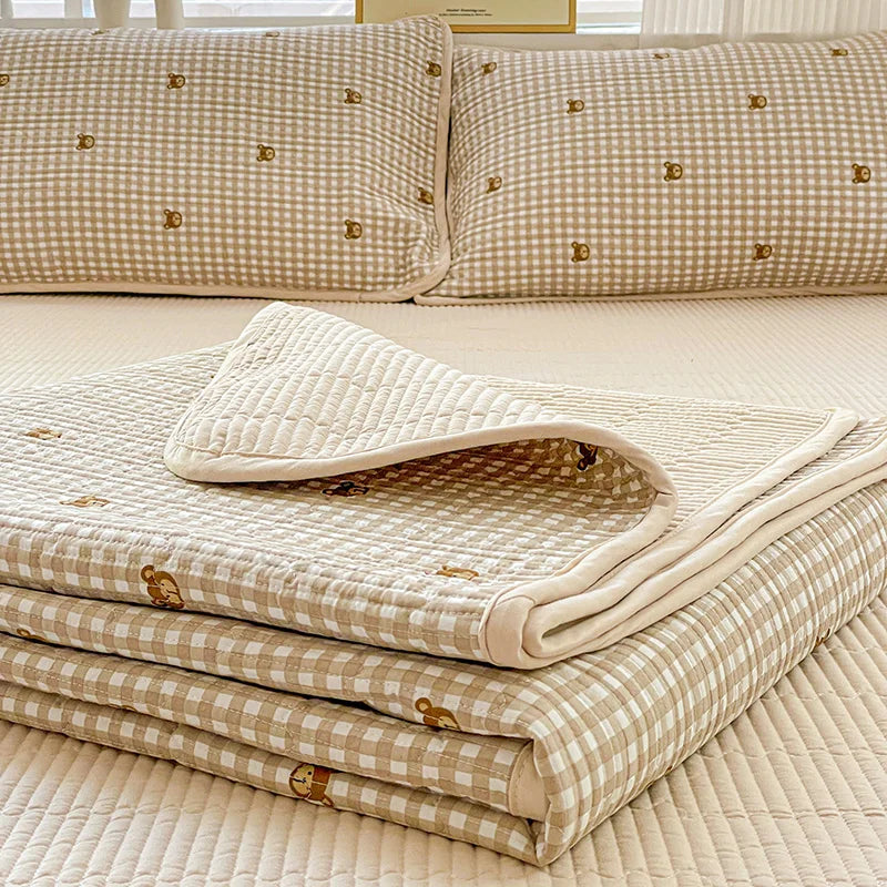 A stack of beige floral quilted bedspreads with gold accents resting on a light yellow surface.
