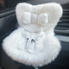 A fluffy white miniature doll seat car vent decoration with a strap detail.