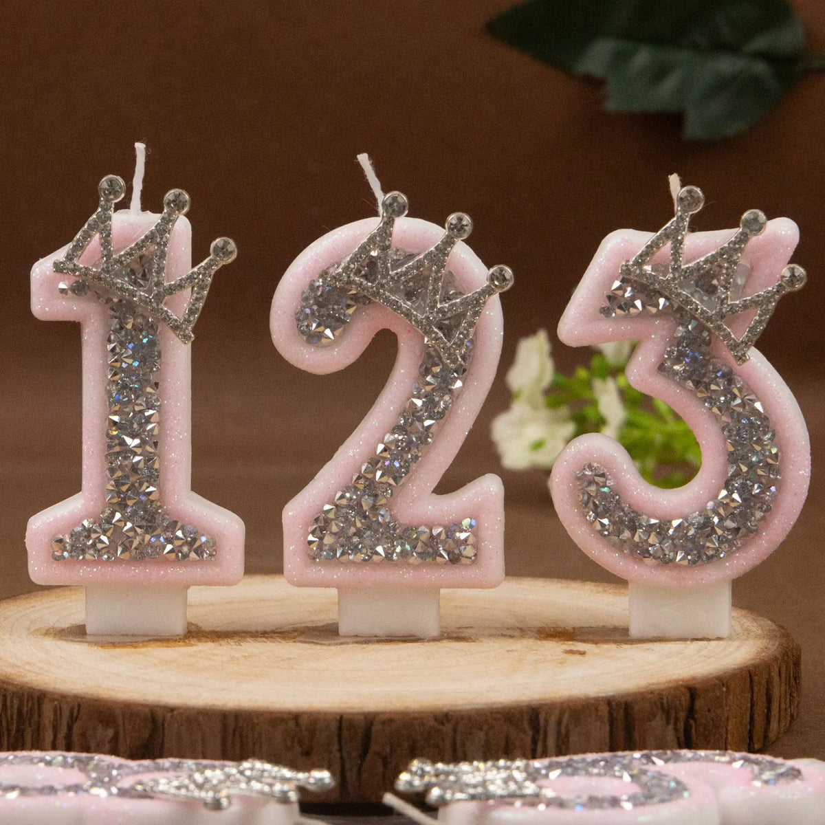 Three pink rhinestone crown number candles 1, 2, and 3 displayed on a wooden surface.