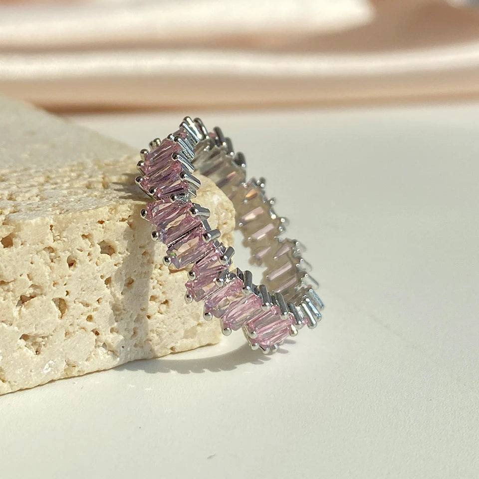 A close-up of a silver ring featuring pink and clear baguette cubic zirconia stones on a light surface.