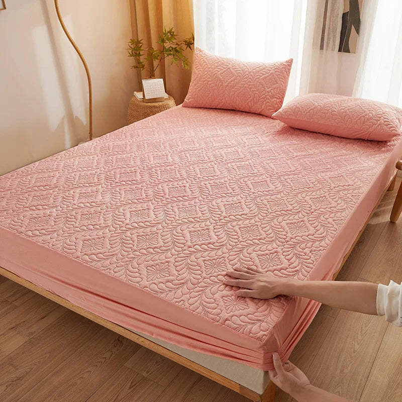 A pink quilted mattress protector is shown being handled on a wooden bed frame.