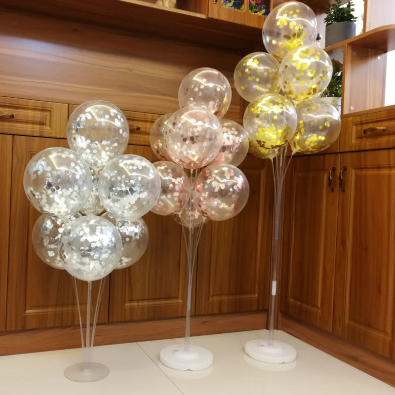 Clear plastic balloon column stands with gold confetti balloons displayed on wooden cabinets.