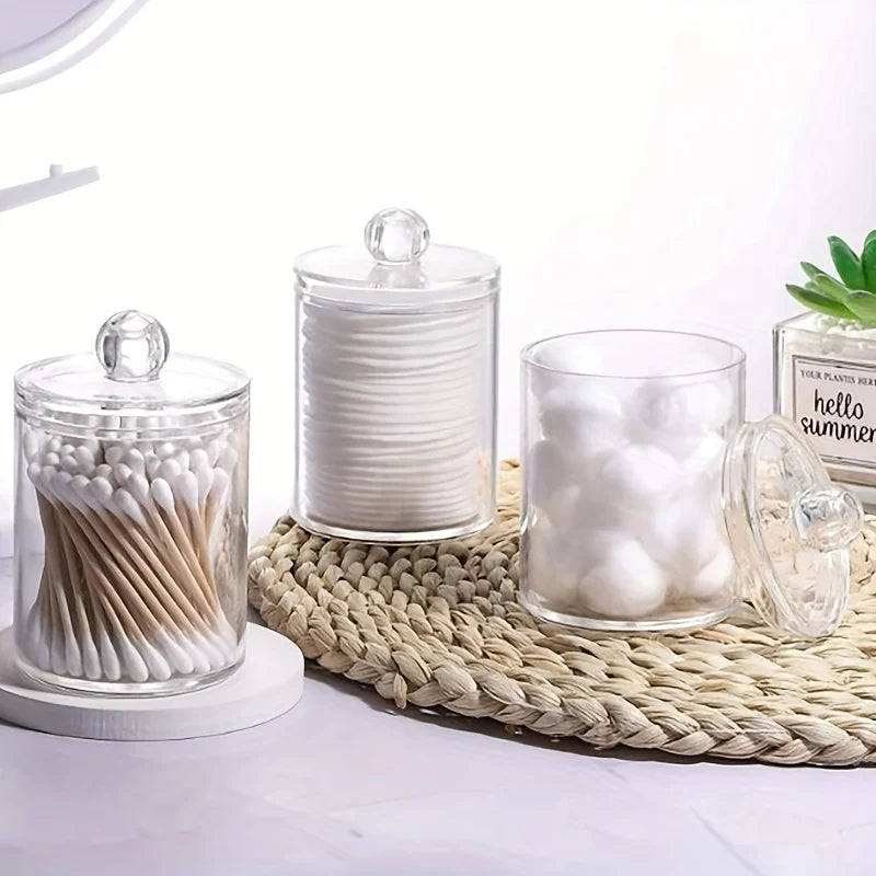 Clear acrylic jar filled with white cotton balls and swabs on a woven mat.