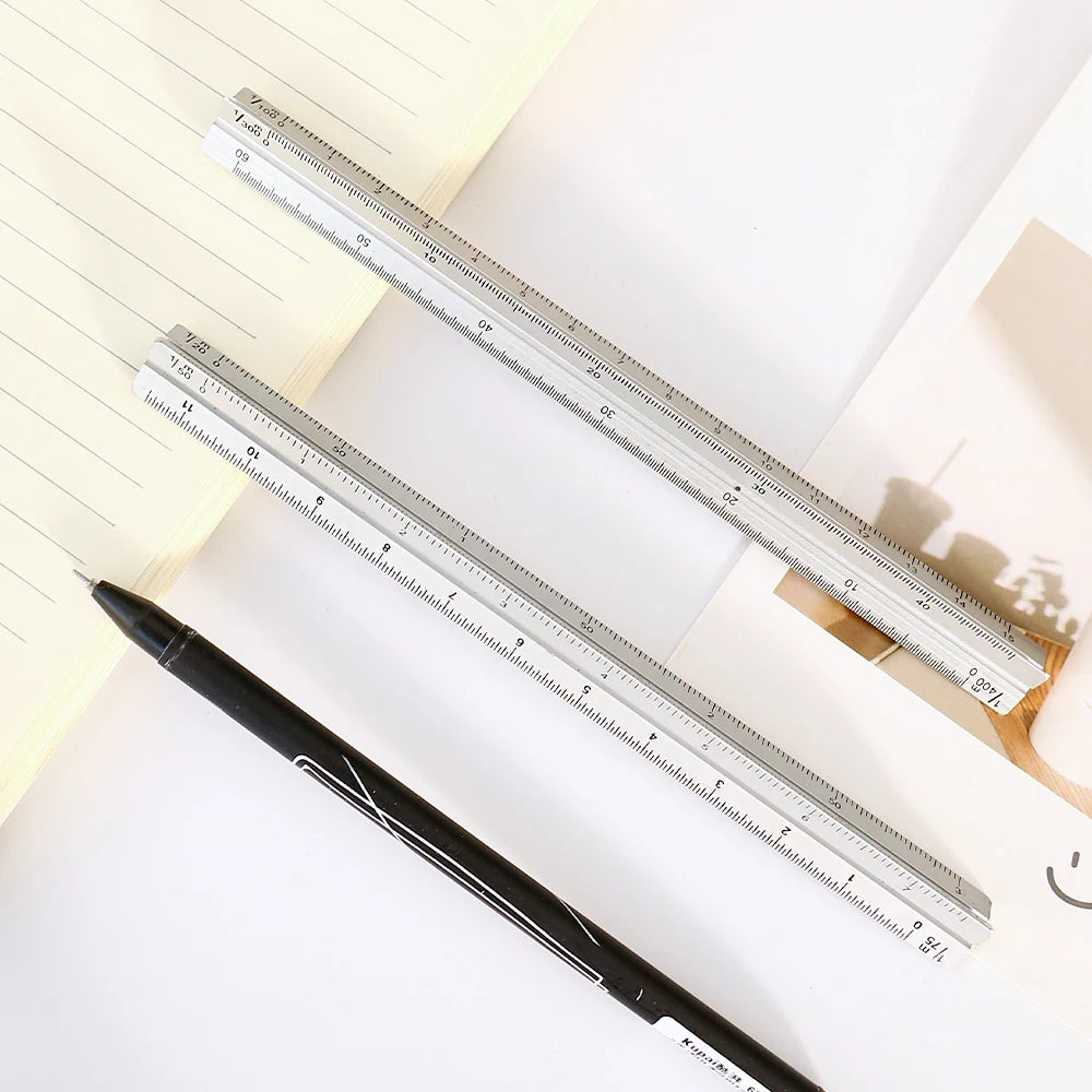 A close-up of an aluminium triangular scale ruler and a black pen resting on a sheet of paper.
