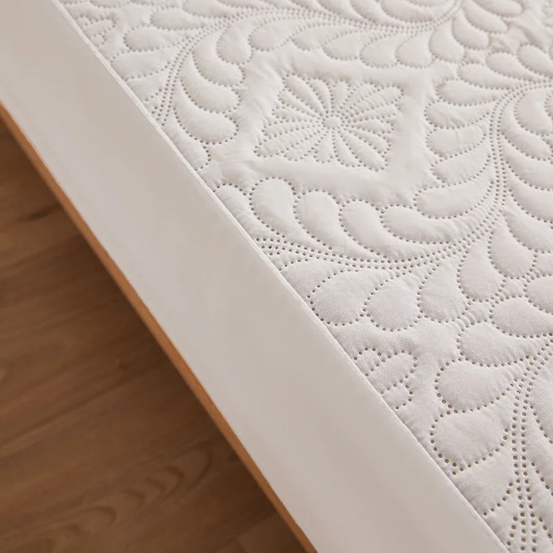 Close-up of a white quilted mattress protector with a decorative pattern on a wooden floor.