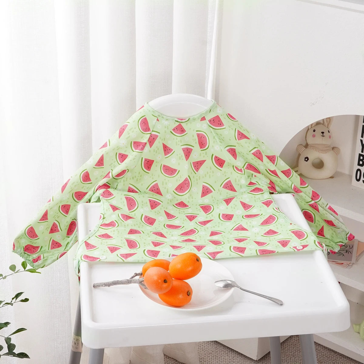 A green long-sleeve waterproof baby bib with a cute animal pattern displayed on a white table.