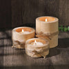 Three rustic wooden tea light holders wrapped with twine sit on a dark surface.
