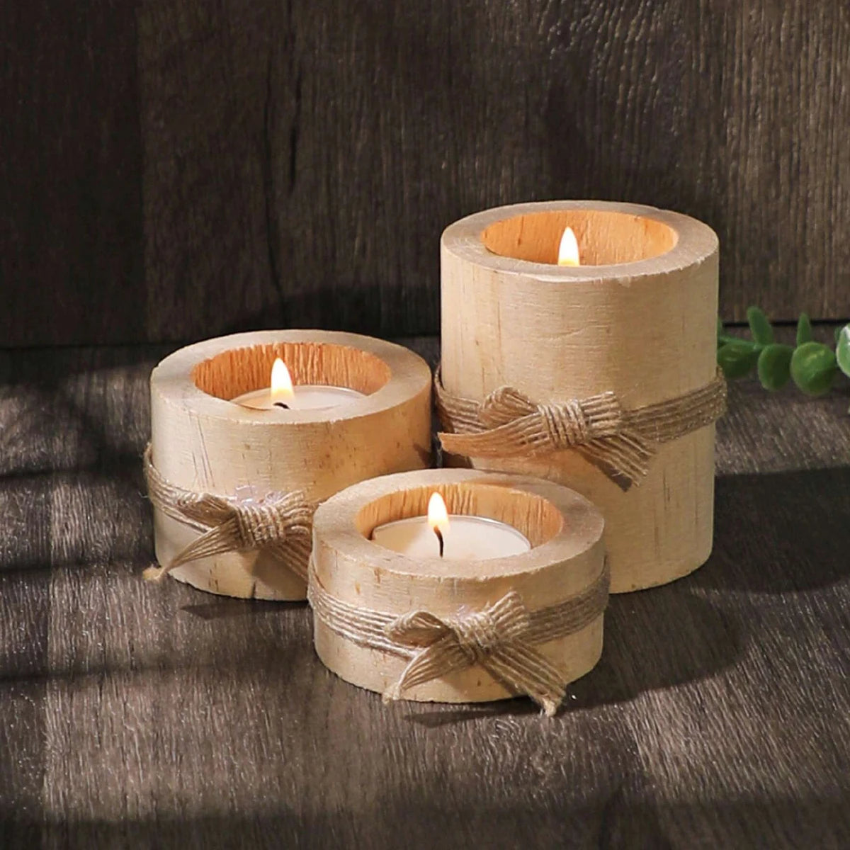 Three rustic wooden tea light holders wrapped with twine sit on a dark surface.