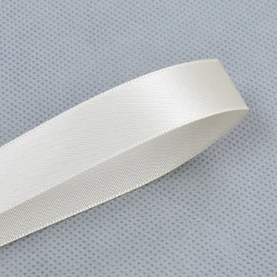 A roll of white double face satin ribbon, shown diagonally on a gray textured surface.