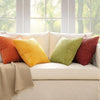A collection of colorful corduroy throw pillows in shades of orange, yellow, green, and red arranged on a light-colored sofa.