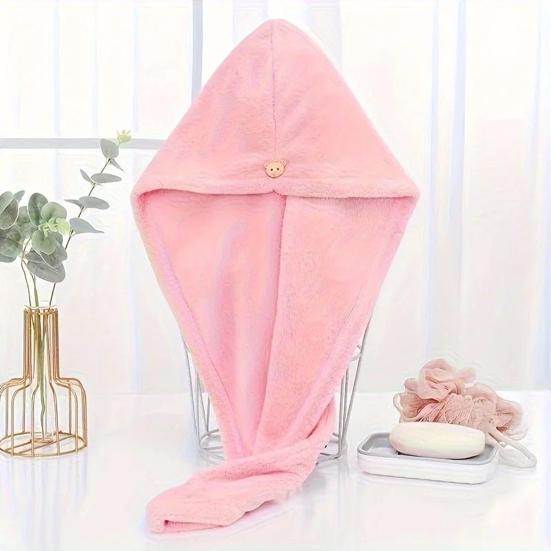 A pink microfiber towel wrap for hair is displayed on a glass stand next to a plant.