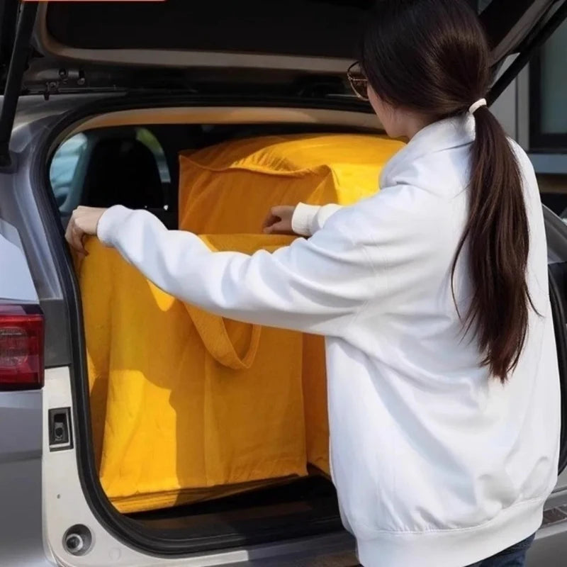 A person is placing a yellow waterproof moving and storage bag into the trunk of a car.