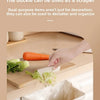 A hand is using a buckle to scrape food scraps into a foldable hanging trash bin in a kitchen setting.