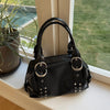A black women's shoulder bag with silver rivet accents resting on a windowsill next to a potted plant.