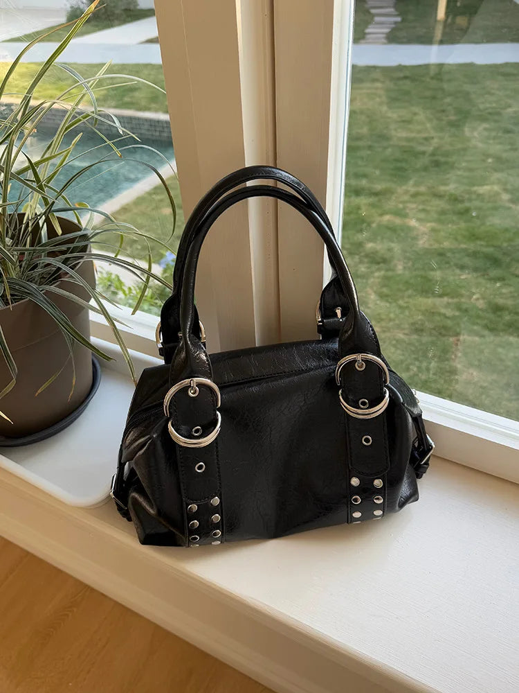A black women's shoulder bag with silver rivet accents resting on a windowsill next to a potted plant.