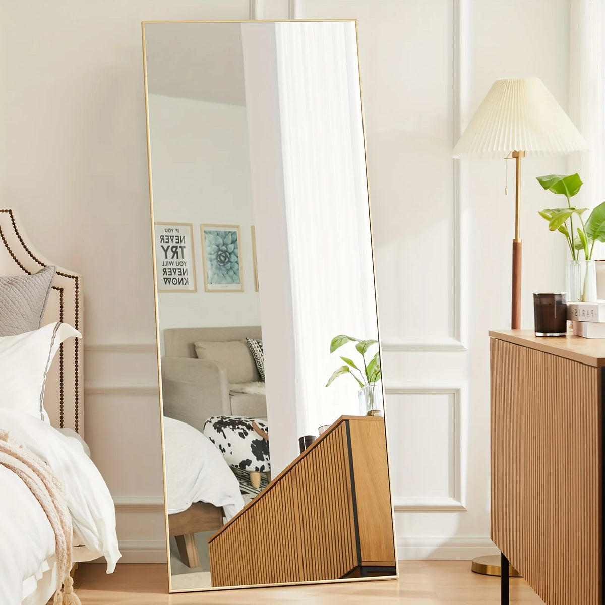 A full-length arched floor mirror with an aluminum frame reflecting a bright interior room.