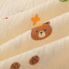 A close-up of a soft cotton gauze baby swaddle blanket featuring a cute brown bear design and small dots.