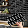 A hand holds a black marble peel and stick tile sticker for kitchen or bathroom backsplash against a black subway tile wall.