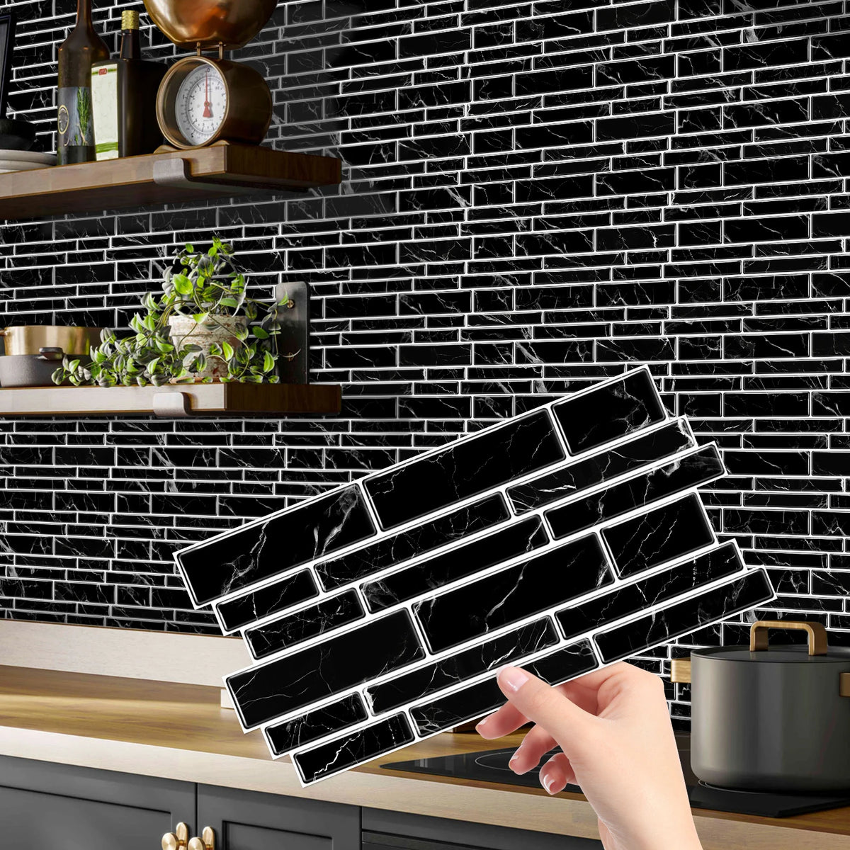 A hand holds a black marble peel and stick tile sticker for kitchen or bathroom backsplash against a black subway tile wall.