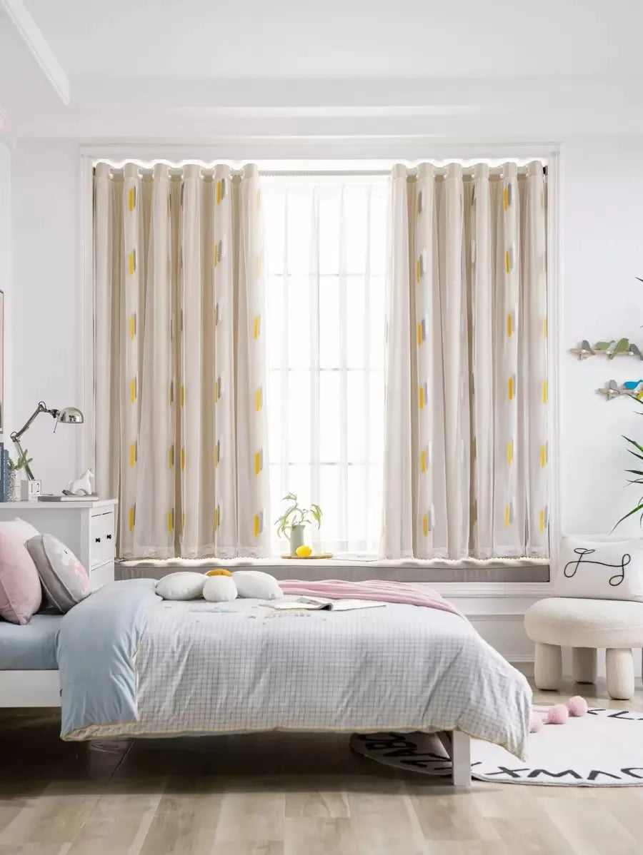 Light beige embroidered curtains with lace trim framing a window in a bright room.
