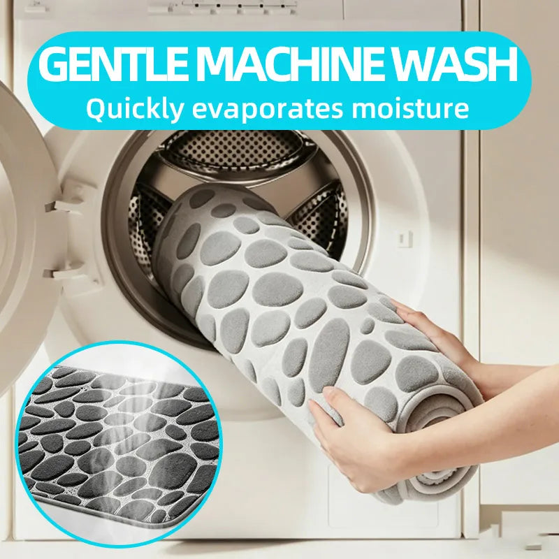 A hand holds a gray plush non-slip absorbent bathroom rug with a pebble texture inside a washing machine drum.
