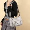 A woman wearing a black sweater and grey top is holding a light silver leather tote bag with an adjustable strap.