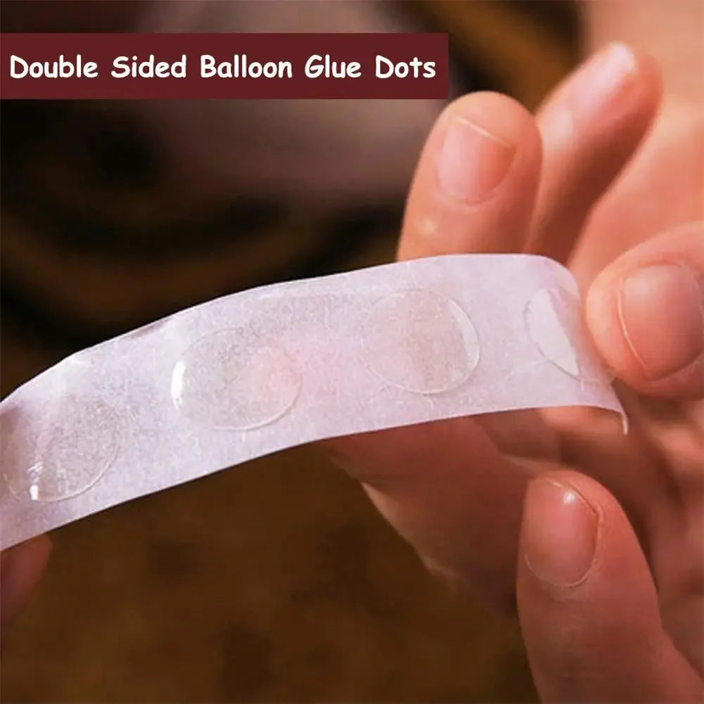 A hand holds a clear double-sided balloon glue dot for crafting or party decoration.