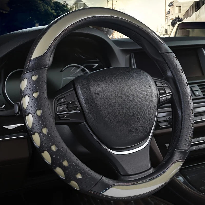 A close-up view of a black steering wheel with heart-shaped patterned leather covers inside a car interior.