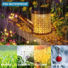 An IP65 waterproof solar watering can garden light with a shepherd's hook illuminating plants in a garden setting.