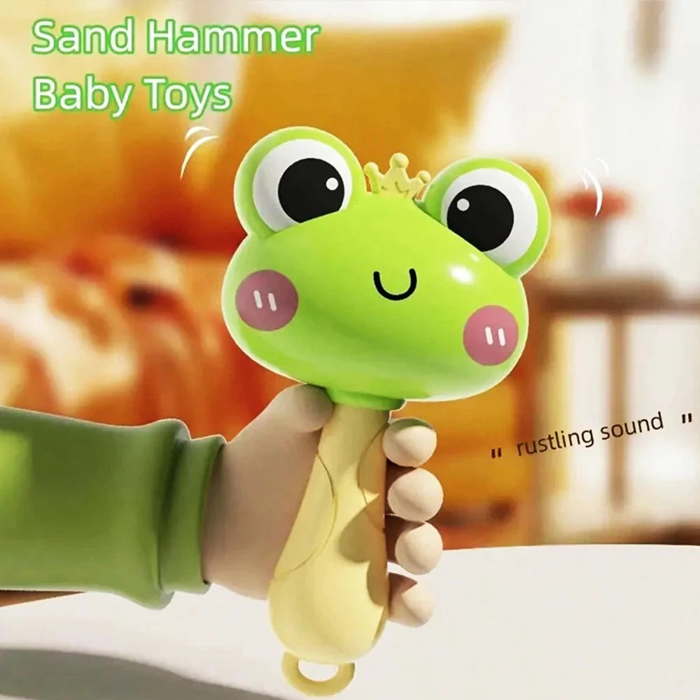 A hand is holding a green cartoon frog baby toy with a crown for a rustling sound sensory grasp toy