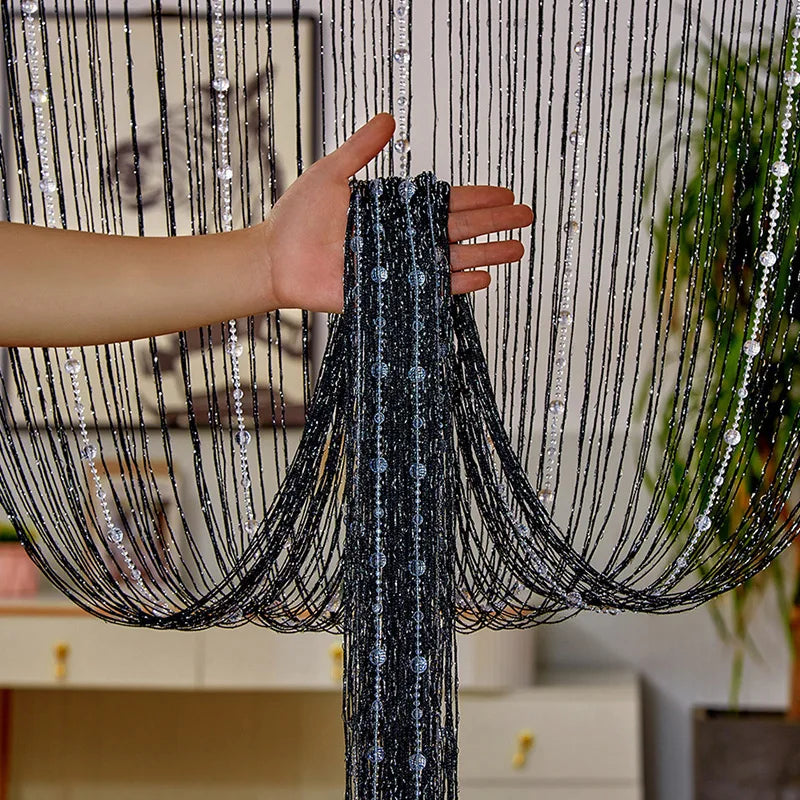 A hand is pulling a black crystal beaded string curtain across a window or doorway.