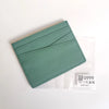 A teal genuine leather slim card holder wallet is shown inside a clear plastic sleeve.