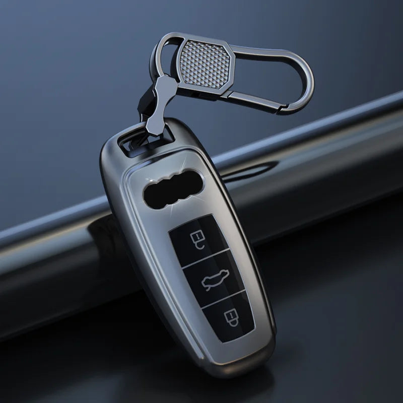 A titanium gray Audi key fob cover with a leather case and a metal loop, shown against a dark background.