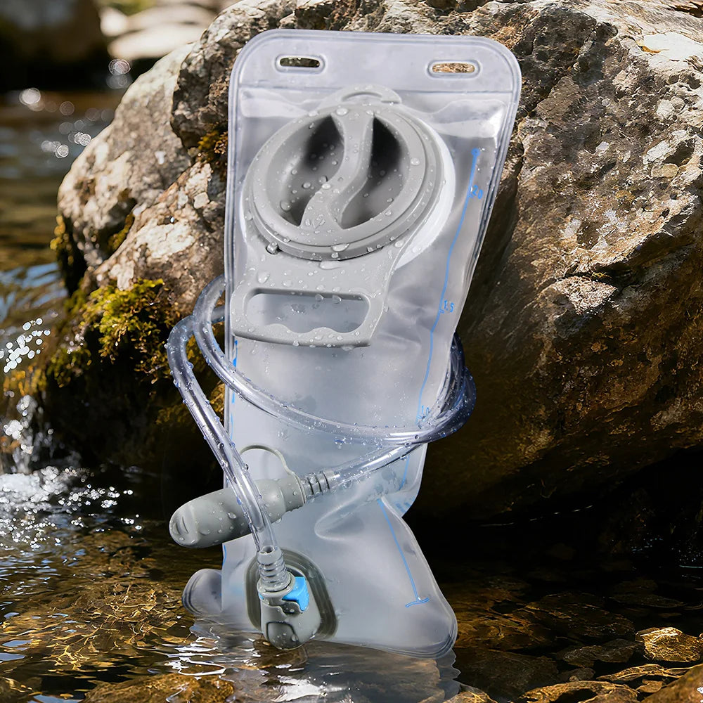 A clear collapsible hydration bladder is submerged in clear water next to a large rock.