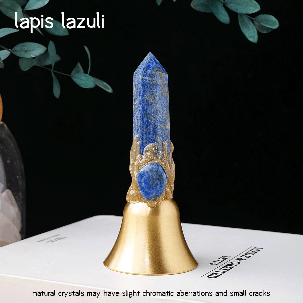 A natural lapis lazuli crystal point mounted on a brass bell, set against a dark background.