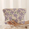 A light purple floral corduroy makeup bag with a zipper is being held by a hand on a white lace surface.