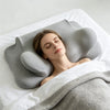 A woman rests her head on a gray memory foam butterfly contour pillow on white bedding.