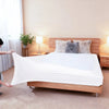 A white stretch-fit box spring cover is displayed on a wooden bed frame with fluffy decorative pillows.