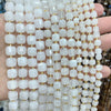 A hand holds a strand of square faceted natural stone beads in white and translucent tones for jewelry making.