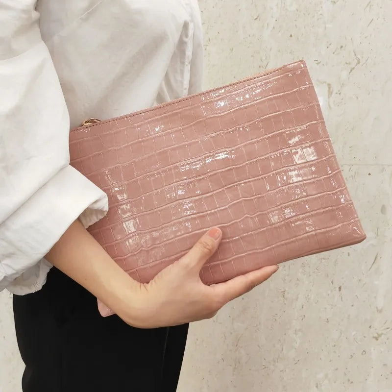 A person holds a pink crocodile-embossed PU leather envelope clutch against a light background.