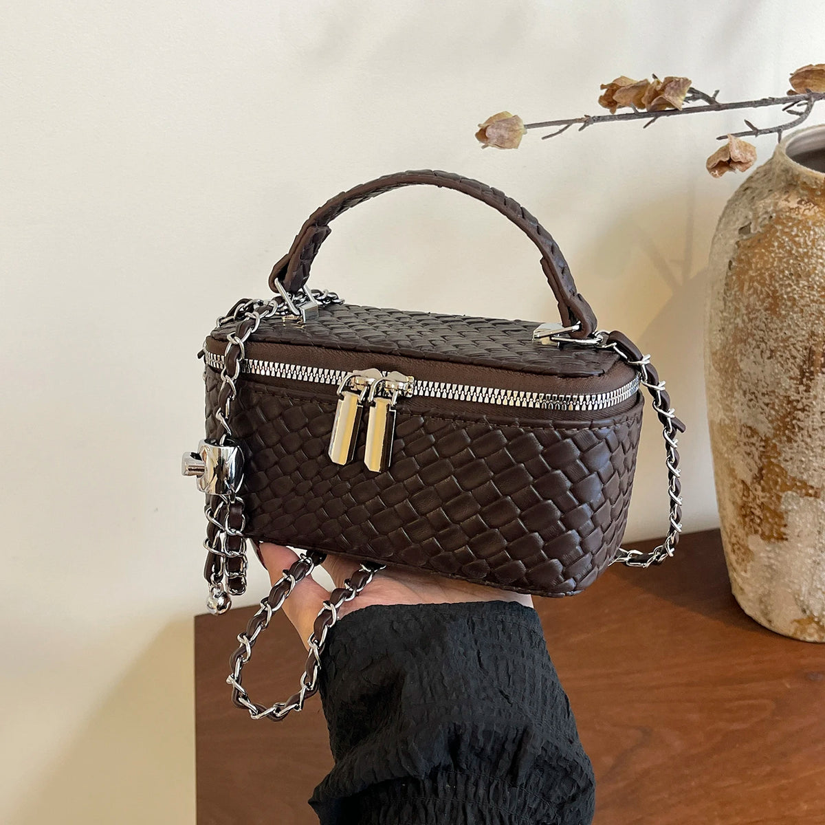 A dark brown woven PU leather crossbody bag with silver chain details is held against a light background.