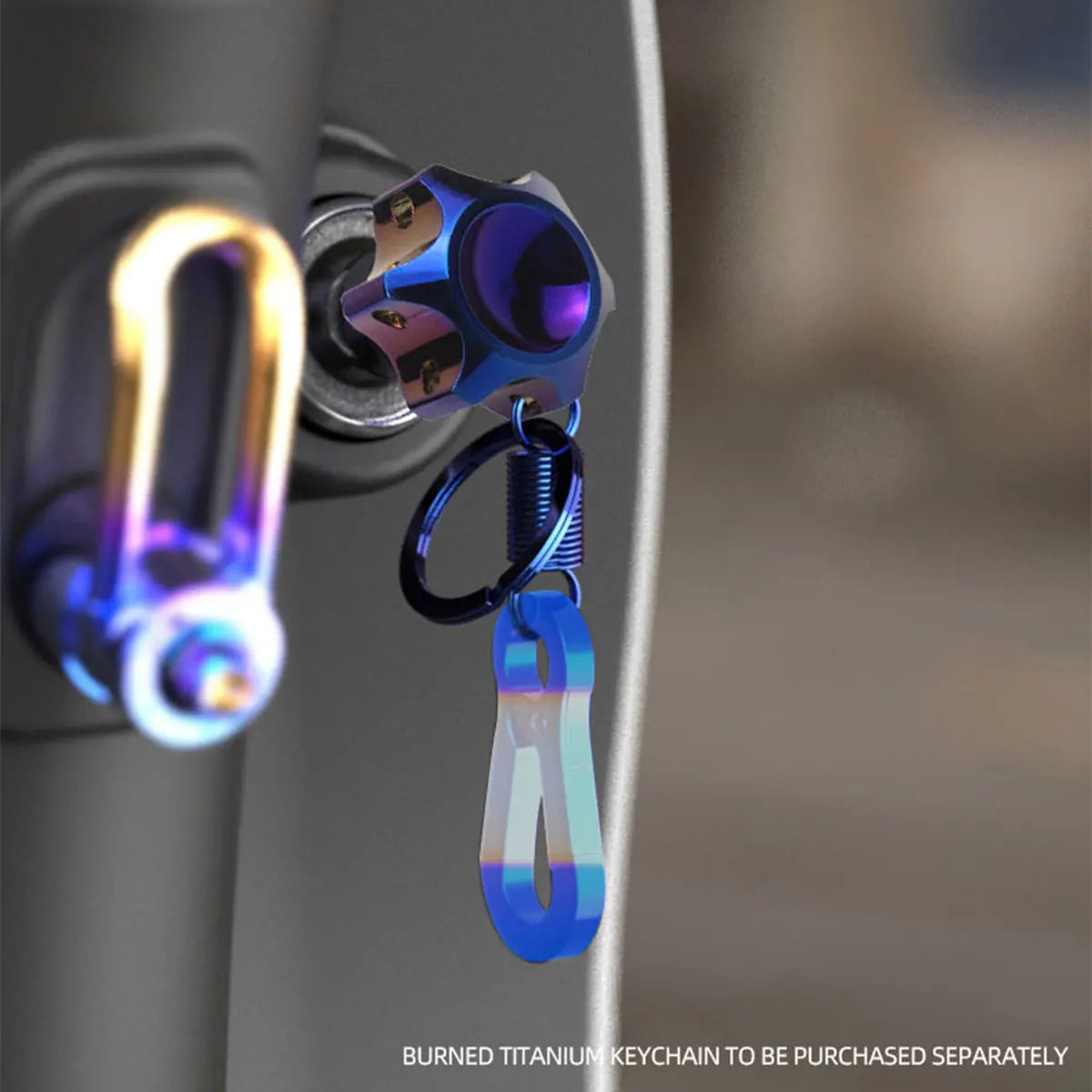 A close-up of a CNC machined titanium motorcycle key head cover keychain with a blue iridescent finish.