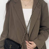 A woman models a dark olive blazer with a gold chain strap for a crossbody bag.
